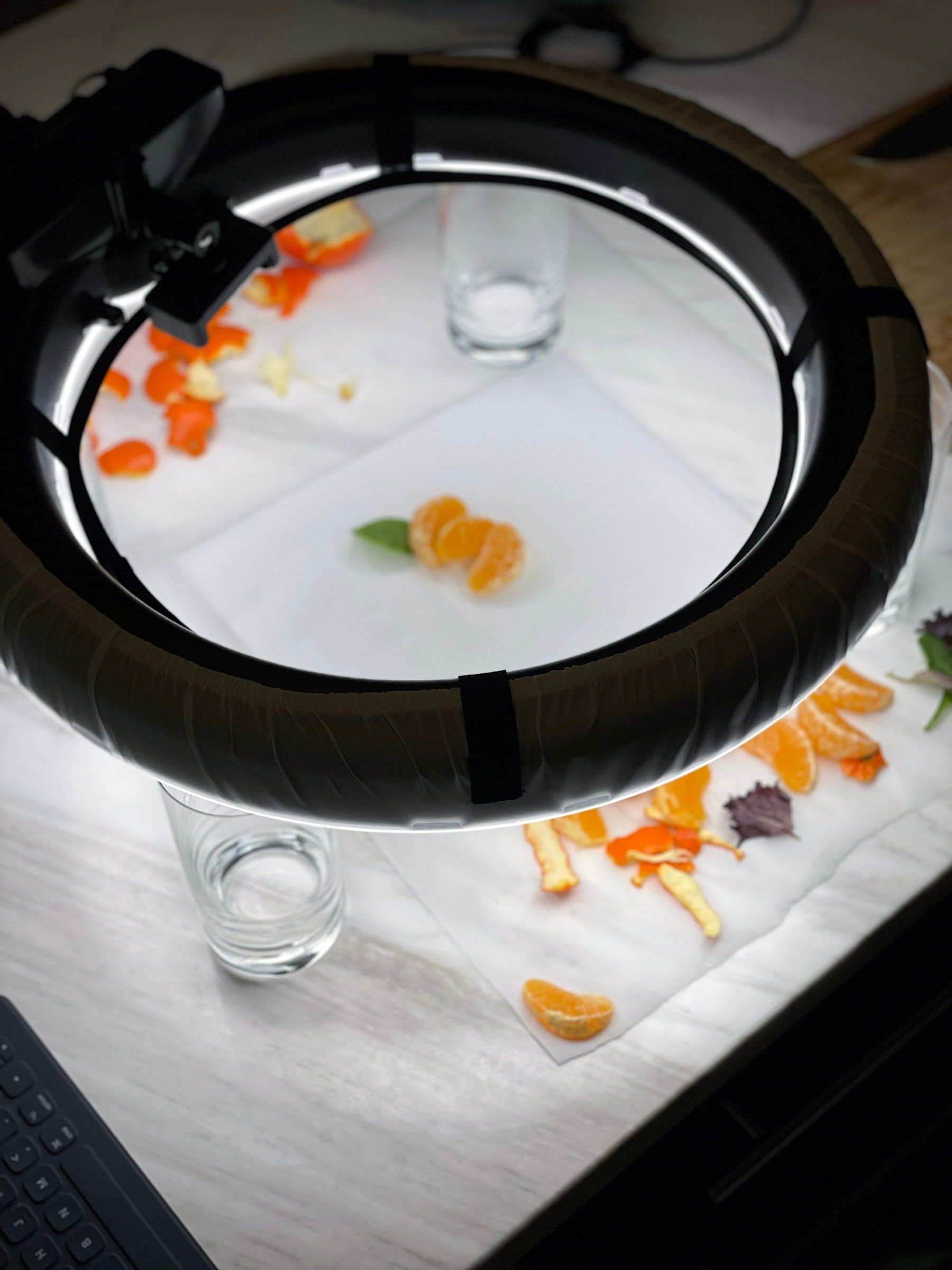 The overhead shooting setup: a ring light over tracing paper, with tangerine segments and leaves arranged and waiting